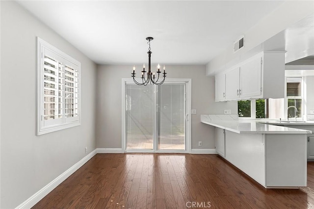kitchen with a peninsula, dark wood-style floors, light countertops, a chandelier, and a sink