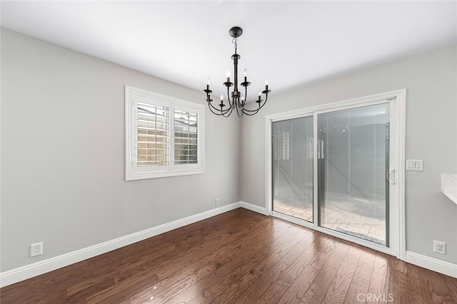 spare room with baseboards, dark wood-type flooring, and a notable chandelier