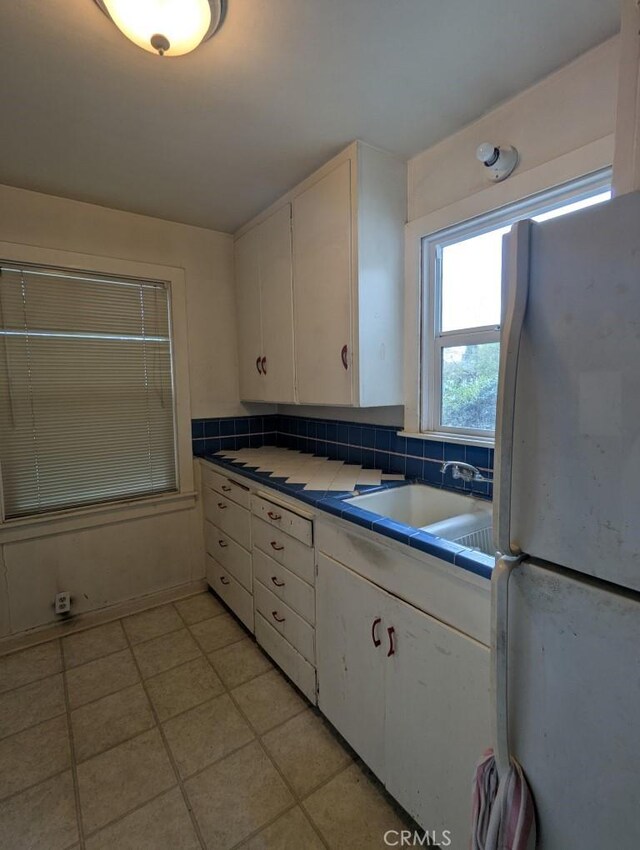548 S Plumas St, Willows, CA 95988 - kitchen with tile counters, light tile patterned floors, white cabinetry, freestanding refrigerator, and a sink