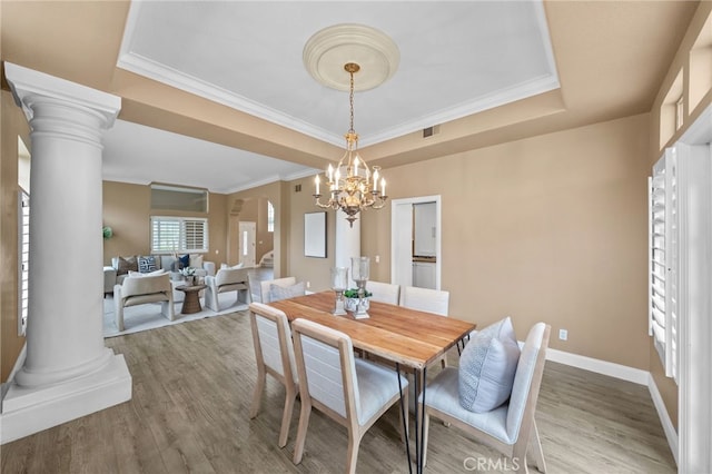 dining area featuring a raised ceiling, ornate columns, a chandelier, and wood finished floors
