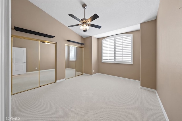 unfurnished bedroom with carpet floors, multiple closets, baseboards, and lofted ceiling