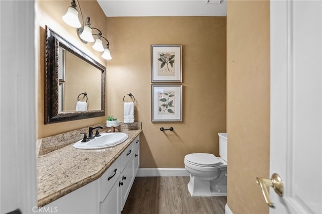 half bath featuring toilet, wood finished floors, vanity, and baseboards