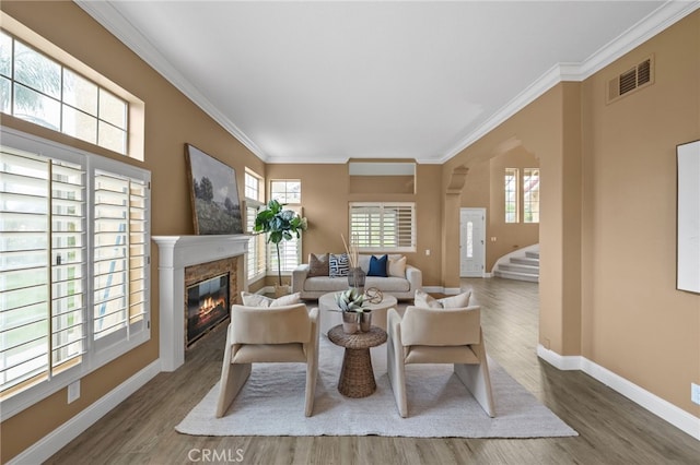 living room featuring a glass covered fireplace, visible vents, ornamental molding, and wood finished floors