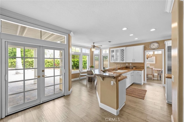 kitchen with a breakfast bar, a peninsula, white cabinetry, crown molding, and a sink