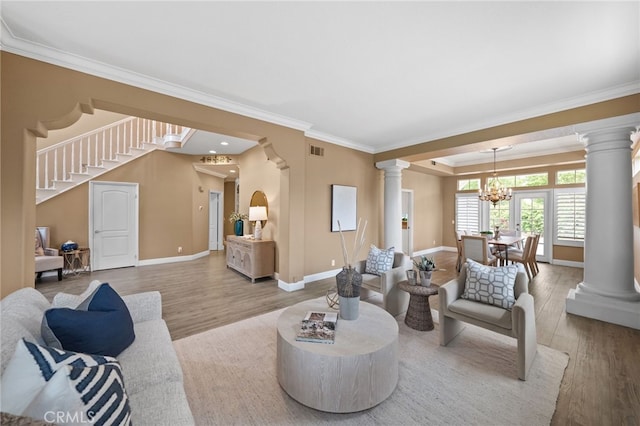 living room featuring a notable chandelier, baseboards, crown molding, decorative columns, and wood finished floors