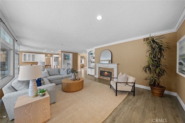 living area featuring baseboards, a warm lit fireplace, ornamental molding, recessed lighting, and wood finished floors