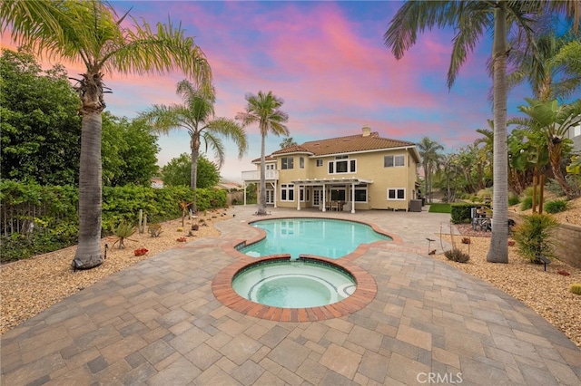 pool at dusk featuring a patio area and a pool with connected hot tub