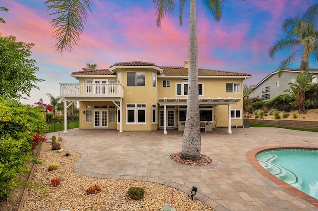 rear view of house with stucco siding, french doors, a patio area, a tiled roof, and fence