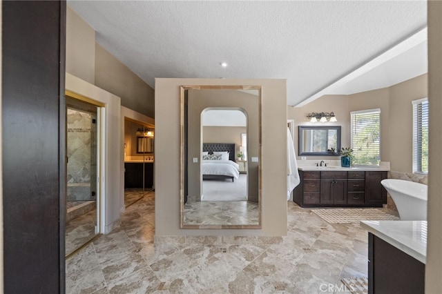 full bath with a textured ceiling, a freestanding tub, vanity, and connected bathroom