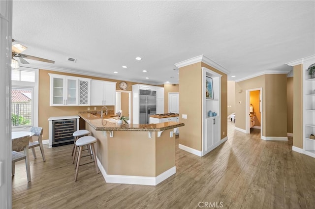 kitchen featuring built in refrigerator, ornamental molding, light wood-style floors, a breakfast bar area, and wine cooler