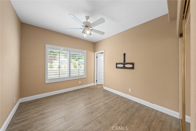 spare room featuring ceiling fan, light wood finished floors, and baseboards