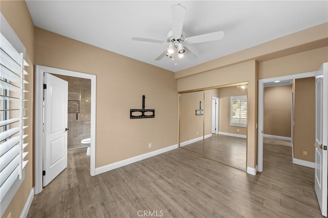 unfurnished bedroom featuring wood finished floors, ensuite bathroom, a closet, and baseboards