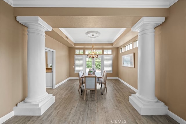 dining room with decorative columns, wood finished floors, and a raised ceiling