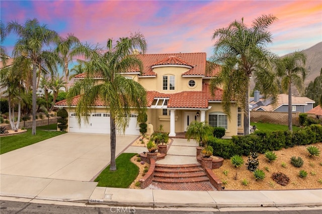 mediterranean / spanish house with a tiled roof, driveway, stucco siding, and fence
