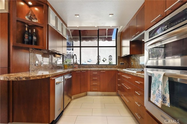 kitchen featuring light tile patterned floors, glass insert cabinets, a sink, stainless steel appliances, and decorative backsplash