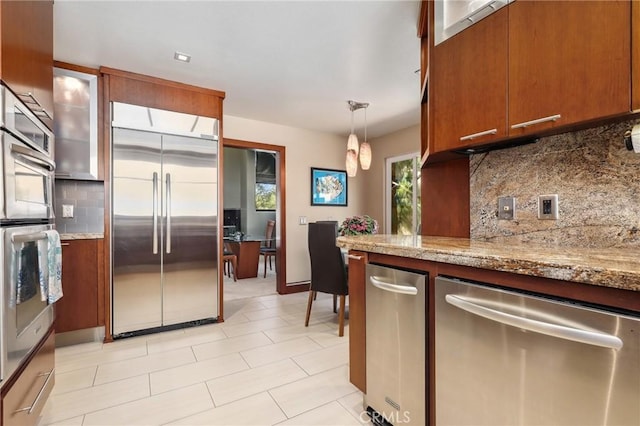 kitchen featuring glass insert cabinets, decorative light fixtures, brown cabinets, stainless steel appliances, and decorative backsplash