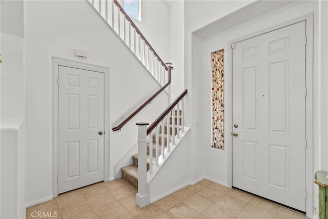 foyer with a high ceiling, light tile patterned floors, baseboards, and stairs