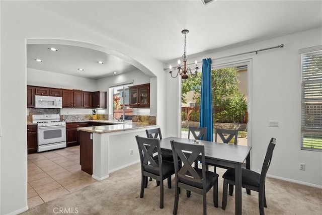 dining space with an inviting chandelier, light tile patterned floors, arched walkways, recessed lighting, and light carpet