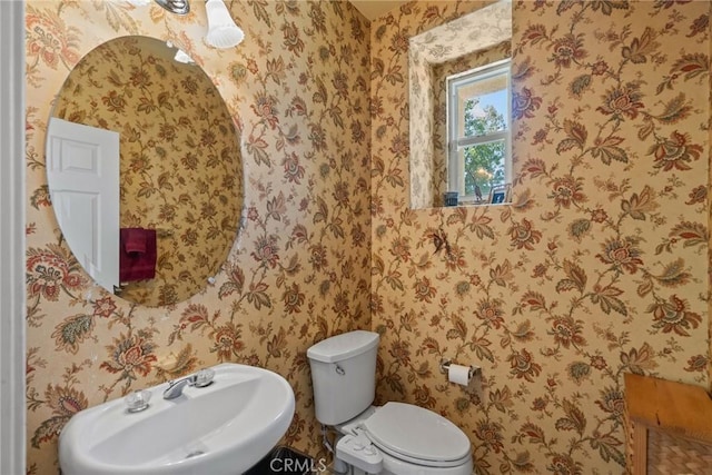 bathroom with toilet, wallpapered walls, and a sink