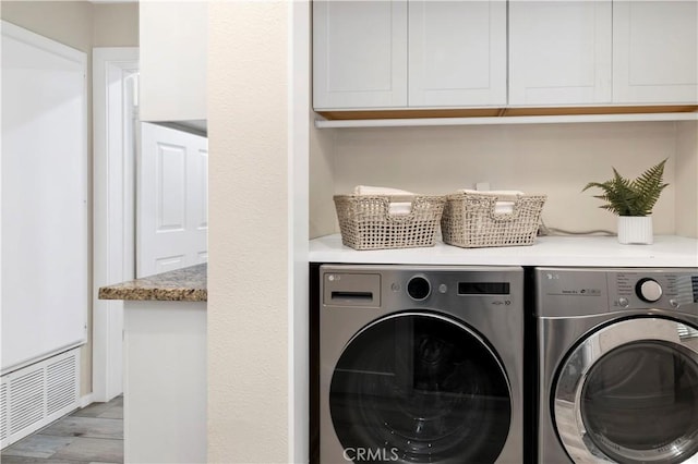 clothes washing area with washing machine and clothes dryer, cabinet space, visible vents, and light wood-type flooring
