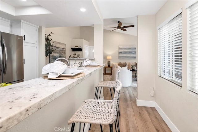 kitchen featuring a ceiling fan, light stone counters, white cabinets, baseboards, and freestanding refrigerator
