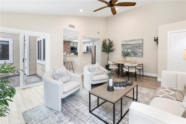 living room featuring vaulted ceiling, a ceiling fan, baseboards, and light wood-type flooring