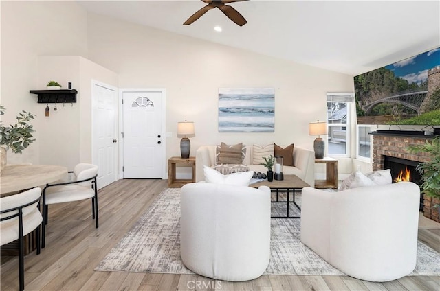 living area featuring vaulted ceiling, wood finished floors, ceiling fan, and a brick fireplace