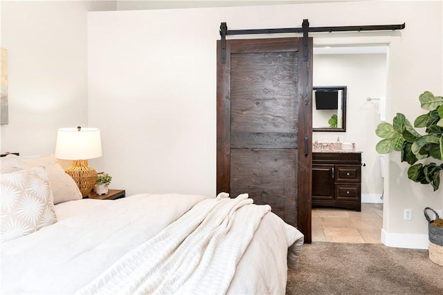 bedroom featuring ensuite bath, a barn door, light carpet, and baseboards