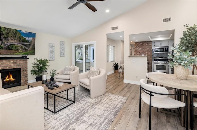 living area featuring a fireplace, light wood-type flooring, visible vents, and ceiling fan