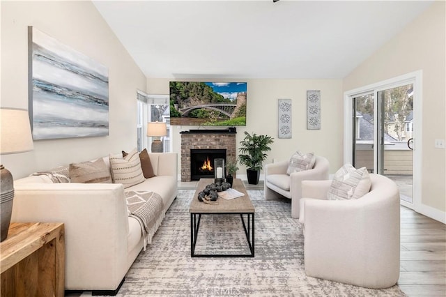 living area with lofted ceiling, a brick fireplace, wood finished floors, and baseboards