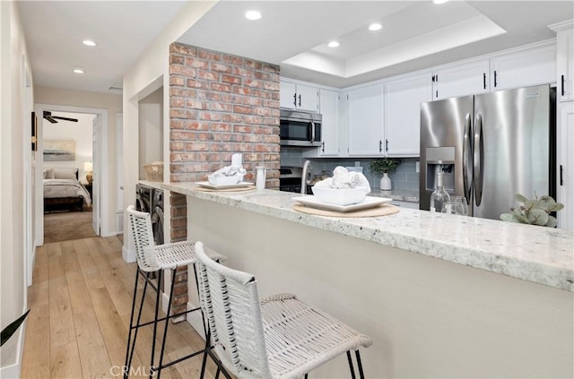 kitchen featuring recessed lighting, appliances with stainless steel finishes, light stone counters, and a raised ceiling