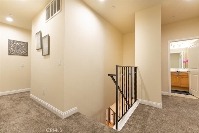 corridor with visible vents, baseboards, carpet, and an upstairs landing