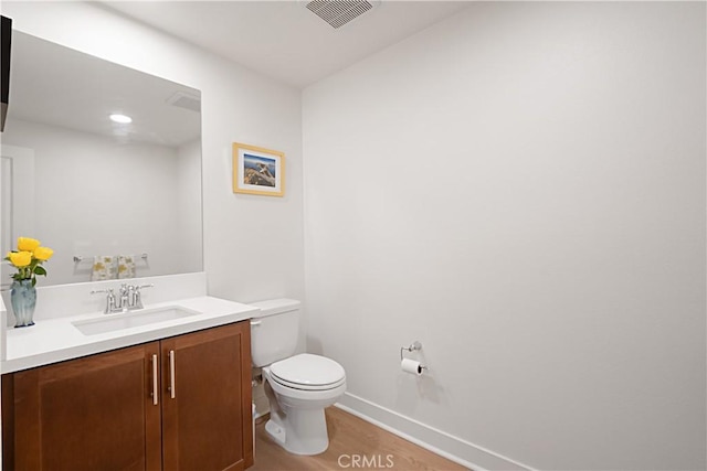 half bathroom with visible vents, baseboards, toilet, wood finished floors, and vanity