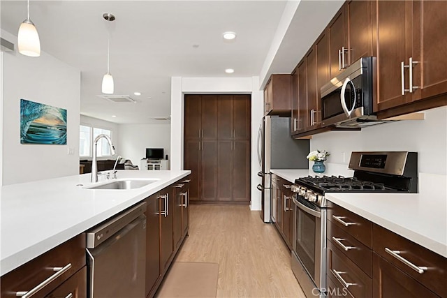 kitchen featuring a sink, stainless steel appliances, light wood-style floors, light countertops, and hanging light fixtures