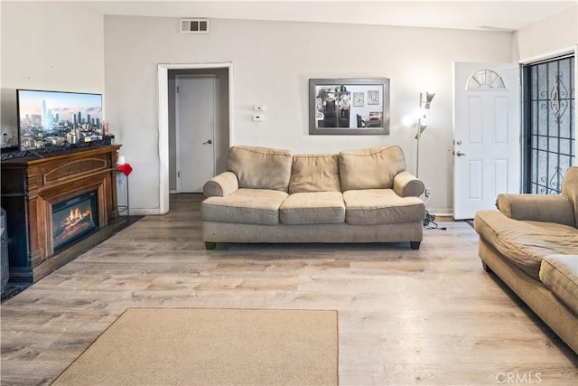 living room featuring a glass covered fireplace, visible vents, baseboards, and wood finished floors