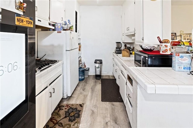 kitchen featuring tile counters, white cabinets, light wood finished floors, and under cabinet range hood