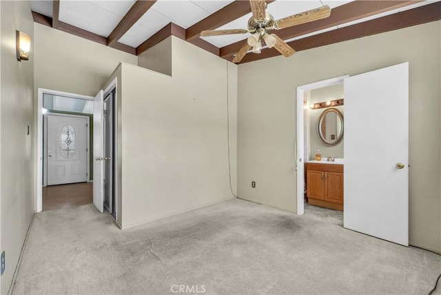 unfurnished bedroom featuring a sink, light colored carpet, beam ceiling, and ensuite bath