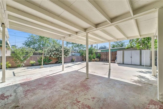 view of patio / terrace featuring a storage unit, a fenced backyard, a carport, and an outdoor structure