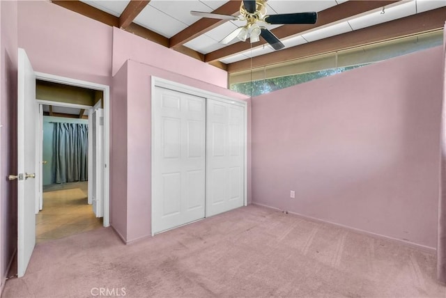 unfurnished bedroom with baseboards, light carpet, beam ceiling, and a closet