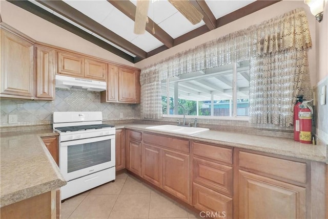 kitchen with decorative backsplash, white gas stove, vaulted ceiling with beams, under cabinet range hood, and a sink