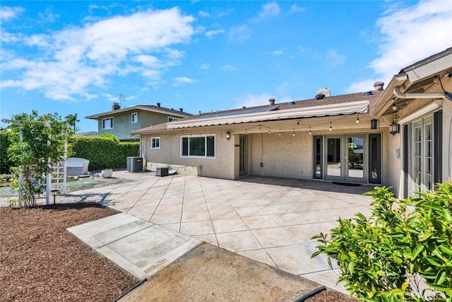 rear view of property featuring central air condition unit, stucco siding, a patio, fence, and french doors