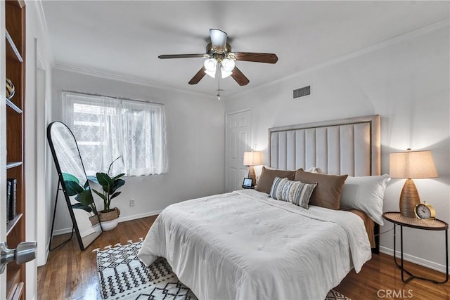 bedroom with wood finished floors, a ceiling fan, visible vents, baseboards, and ornamental molding