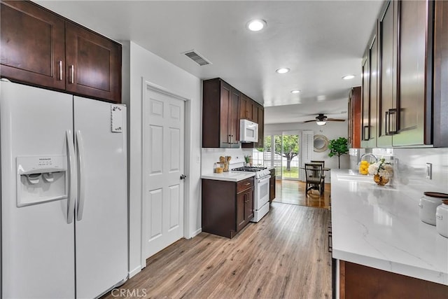 kitchen featuring a ceiling fan, a sink, light wood-type flooring, visible vents, and white appliances