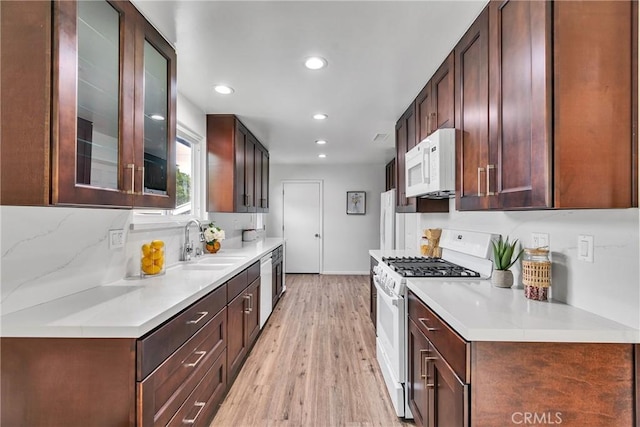 kitchen featuring a sink, white appliances, light wood-type flooring, recessed lighting, and glass insert cabinets
