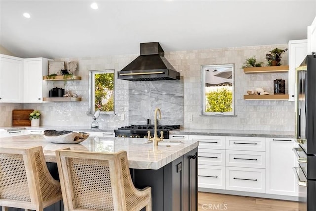 27553 Via Fortuna, San Juan Capistrano, CA 92675 - kitchen featuring wall chimney range hood, light stone counters, open shelves, and black refrigerator