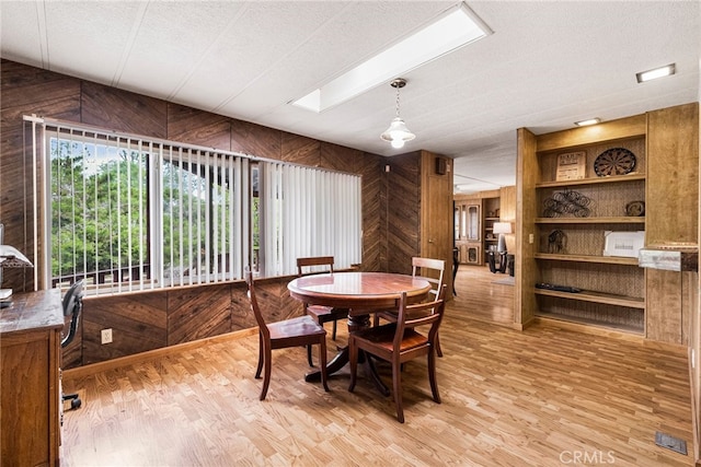 dining room featuring light wood-type flooring, wooden walls, a textured ceiling, and a skylight