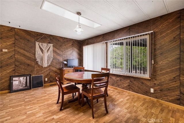 dining area featuring wooden walls, a skylight, light wood-type flooring, and a textured ceiling