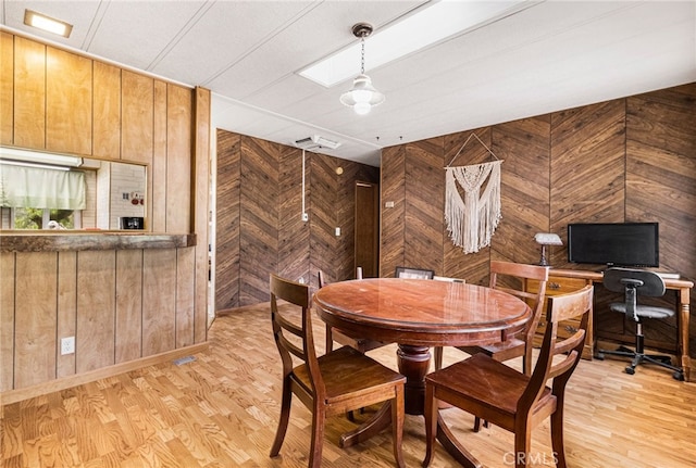 dining room featuring wood walls, light wood finished floors, and visible vents
