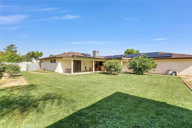 back of property featuring fence, a yard, a patio, stucco siding, and solar panels