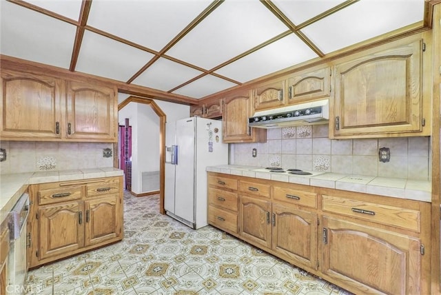 kitchen featuring brown cabinets, under cabinet range hood, backsplash, and white appliances